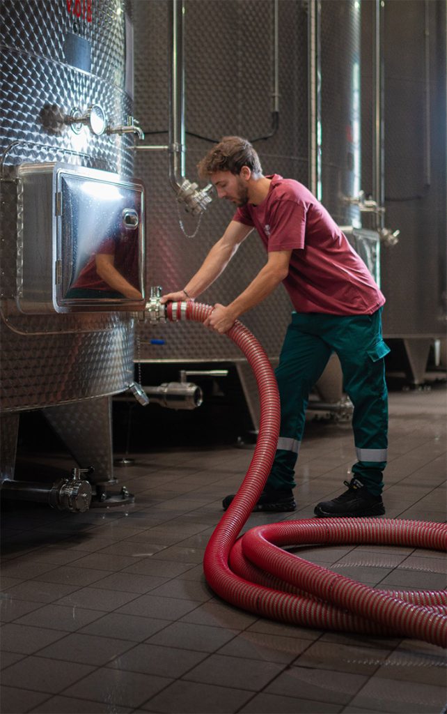 About us | Cesari | identity winery operator racking wine from one stainless steel container to anther with a red pump